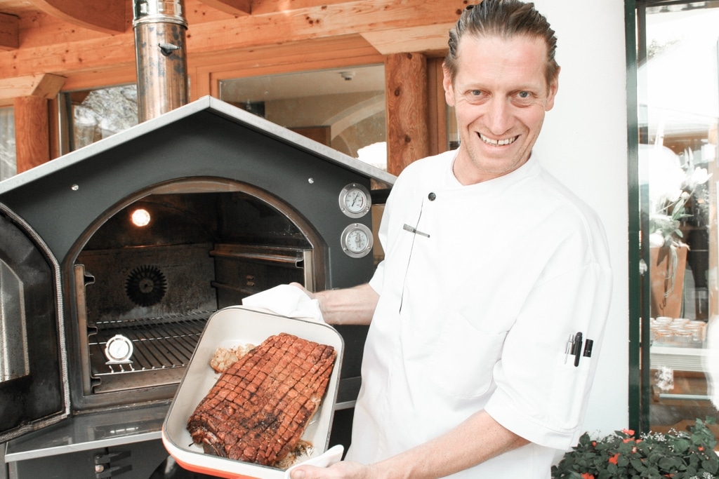Küchenchef Jürgen Archam mit Schweinsbraten vor dem Holzhofen